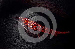 Macro and close-up creative make-up theme: beautiful female eye with black skin and red diamonds, retouched photo