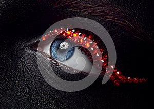 Macro and close-up creative make-up theme: beautiful female eye with black skin and red diamonds, retouched photo