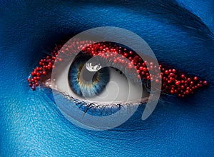 Macro and close-up creative make-up theme: Beautiful female eye with blue paint on face and small red balls of caviar