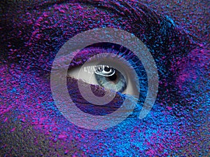 Macro and close-up creative make-up theme: Beautiful female eye with dry paint dust pigment on face, purple and blue color