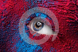 Macro and close-up creative make-up theme: Beautiful female eye with dry paint dust pigment on face, red and blue color