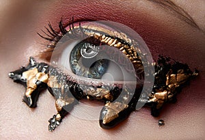 Macro and close-up creative make-up theme: beautiful female eye with red shadows and gold, black paint, retouched photo
