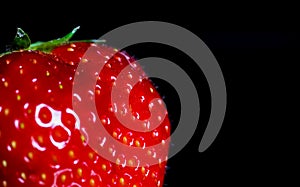 Macro close up of one single isolated ripe red strawberry with green leaves on black reflecting glass plate illuminated by studio