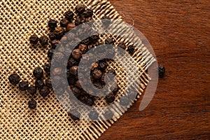 Macro close-up of Organic Black pepper Piper nigrum on wooden top background and jute mat. Pile of Indian Aromatic Spice.