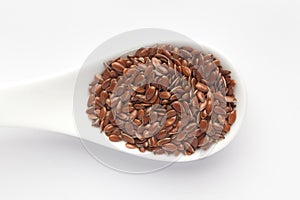 Macro Close up of  Organic Brown flaxseeds Linum usitatissimum or linseed on a white ceramic soup spoon. photo