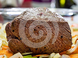 Macro close-up of a roast topside of beef on a bed of vegetables