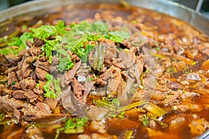 Macro close up shot of Pork stewed in the gravy with green coriander leaves on top and soup.