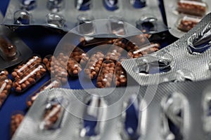 Macro close up of silver empty blisters with pile of capsules, blue background - medicines waste abuse concept