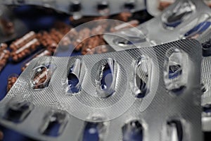 Macro close up of silver empty blisters with pile of capsules, blue background - medicines waste abuse concept