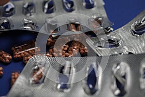 Macro close up of silver empty blisters with pile of capsules, blue background - medicines waste abuse concept