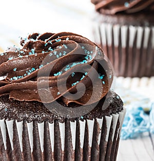 A macro close up view of a chocolate cupcake with chocolate frosting and blue sprinkles ready for eating.