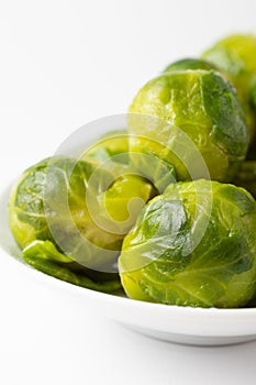 Macro closeup of green Brussels sprouts on white plate, white background, vertical