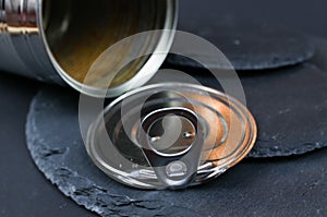 Macro closeup of isolated shiny metal food can with lid on black slate stone background