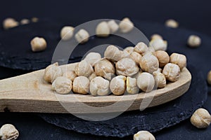 Macro closeup of isolated wood spoon with raw uncooked chickpeas channa dhal on black slate stone background