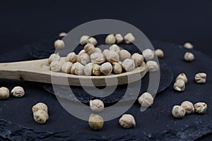 Macro closeup of isolated wood spoon with raw uncooked chickpeas channa dhal on black slate stone background
