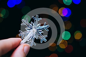 Macro closeup shot of fingers holding a Christmas light in a snowflake design