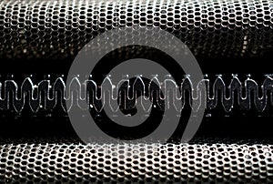 Macro detail of black and silver head of a shaving machine with its sharp razor blades behind the perforated metal grid