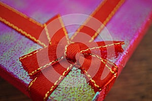 Macro detail of a red ribbon with golden stitching wrapping a pink christmas present