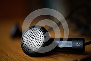 Macro detail of a silver and black perforated headphones (ear-buds) with cables