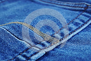 Macro detail of a yellow thread stitching typical blue men`s jeans