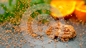 MACRO, DOF: Small round seeds fall and bounce next to a dollop of mustard.