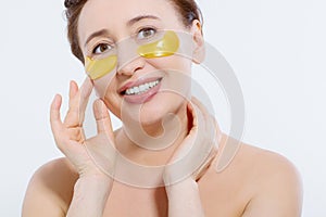 Macro female face. Beauty portrait of middle age woman with wrinkles and a gold patch under eye isolated on white background.