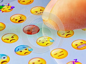 Macro finger touching angry emoji on a virtual keyboard