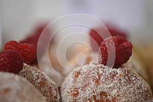 Macro food photography of delicious homemade sugar coated jam doughnuts with a fresh fruit raspberry on top