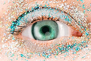 Macro green female eye with glitter eyeshadow, colorful sparks, crystals. Beauty background, fashion glamour makeup