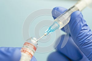 Macro of a hypodermic syringe or needle being filled with mRNA vaccine from bottle against blue background
