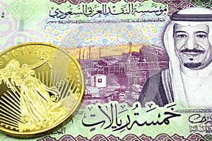A Saudi Arabian riyal bill with a gold coin close up photo