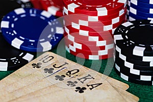 A macro image of a Royal Club Flush on a deck of vintage used cards surrounded by red, blue and black betting chips on a green