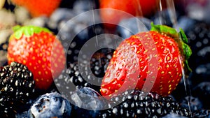 Macro image of water dropelts falling on fresh strawberries, blueberries and blackberries. Rain over ripe berries