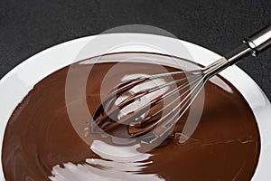 Macro of Melted milk or dark chocolate swirl in plate and whisk on concrete background