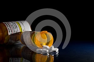 Macro of oxycodone opioid tablets with prescription bottles against dark background