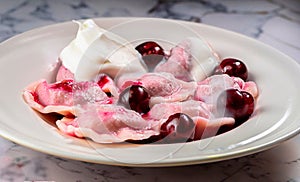 macro photo of cherry dumplings covered with sour cream with steam in a plate on a white mar