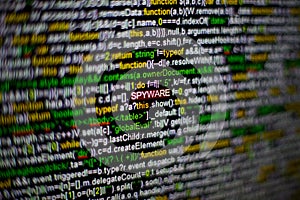 Macro photo of computer screen with program source code and highlighted SPYWARE inscription in the middle. Script on the