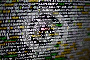 Macro photo of computer screen with program source code and highlighted TROJAN inscription in the middle. Script on the