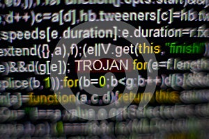 Macro photo of computer screen with program source code and highlighted TROJAN inscription in the middle. Script on the