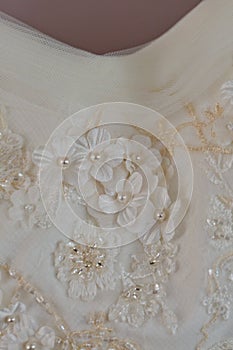 A macro photo of a detailed white wedding dress with white flowers and fake diamonds knitted to the dress