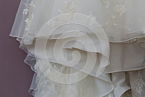 A macro photo of a detailed white wedding dress with white flowers and fake diamonds knitted to the dress