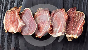 macro photo of dried sliced lamb meat on black wooden surface top view
