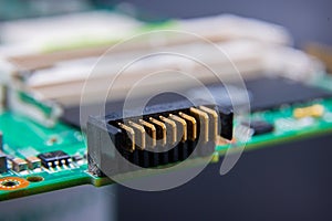 Macro photo of gold plated connectors on a green computer circuit board, with RAM connector in the background