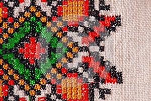 Macro photo of linen fabric with red, green, black and orange embroidery. Fabric as a background