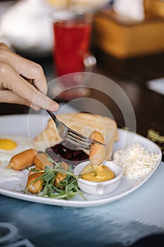 Macro photo of man slice sausage and dips it in mustard. English breakfast outdoor. Lunch in restaurant. Food