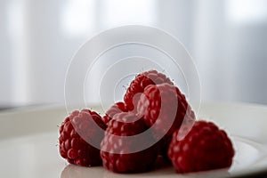 Macro photo of red raspberries on a white plate against neutral background. Simple food for a break, healthy lifestyle