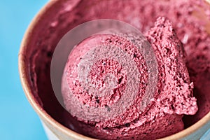 Macro photo of scoop of frozen berry ice cream in a paper glass on a blue background. Top view