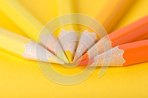 Macro photograph of several pencils of yellow and orange color on a paper background