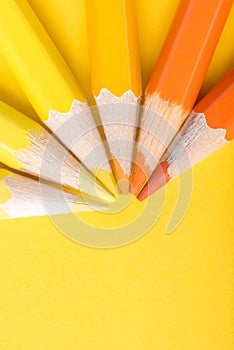 Macro photograph of several pencils of yellow and orange color on a paper background