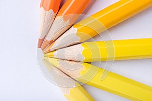 Macro photograph of several pencils of yellow and orange color on a white background